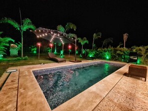 A swimming pool with lounge chairs and a pergola with string lights. - Villas María Salomé (La Romana)