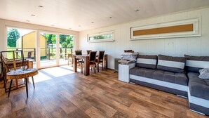 Un vaste espace de vie doté d’un plancher en bois, d’un canapé, d’une table à manger avec des chaises et d’une porte-fenêtre coulissante donnant sur un patio extérieur.