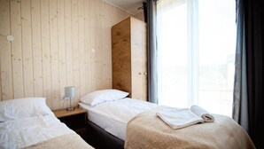 Une chambre avec deux lits, des murs en bois, une table de chevet avec une lampe et une fenêtre avec des rideaux.