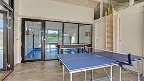 A ping pong table in a modern indoor space with glass doors leading to an outdoor area. - Cozy home in Ejstrupholm (Ejstrupholm)