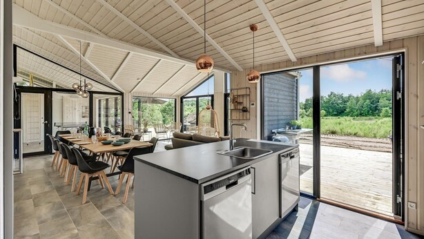 A modern kitchen with a large island, a dining area with chairs, and a view of the outdoors. - Cozy home in Ejstrupholm (Ejstrupholm)