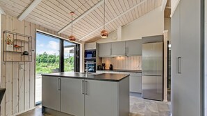 A modern kitchen with a large island, stainless steel appliances, and a view of greenery outside. - Cozy home in Ejstrupholm (Ejstrupholm)
