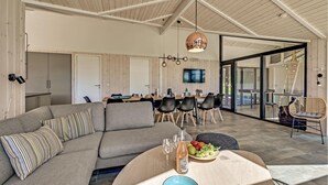 A spacious living area with a grey sofa, a dining table with chairs, a large TV, and a wicker chair. - Cozy home in Ejstrupholm (Ejstrupholm)
