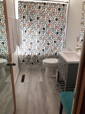 Bathroom features a white toilet, sink, and mirror, set against a geometric-patterned backdrop.