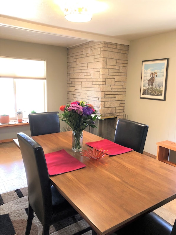 Enjoy meals in this cozy dining area with a table for four, a vase of flowers, and a fireplace in the background.