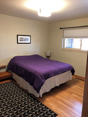Relax in a spacious bedroom with a large bed, a framed picture, and a window with a blind.