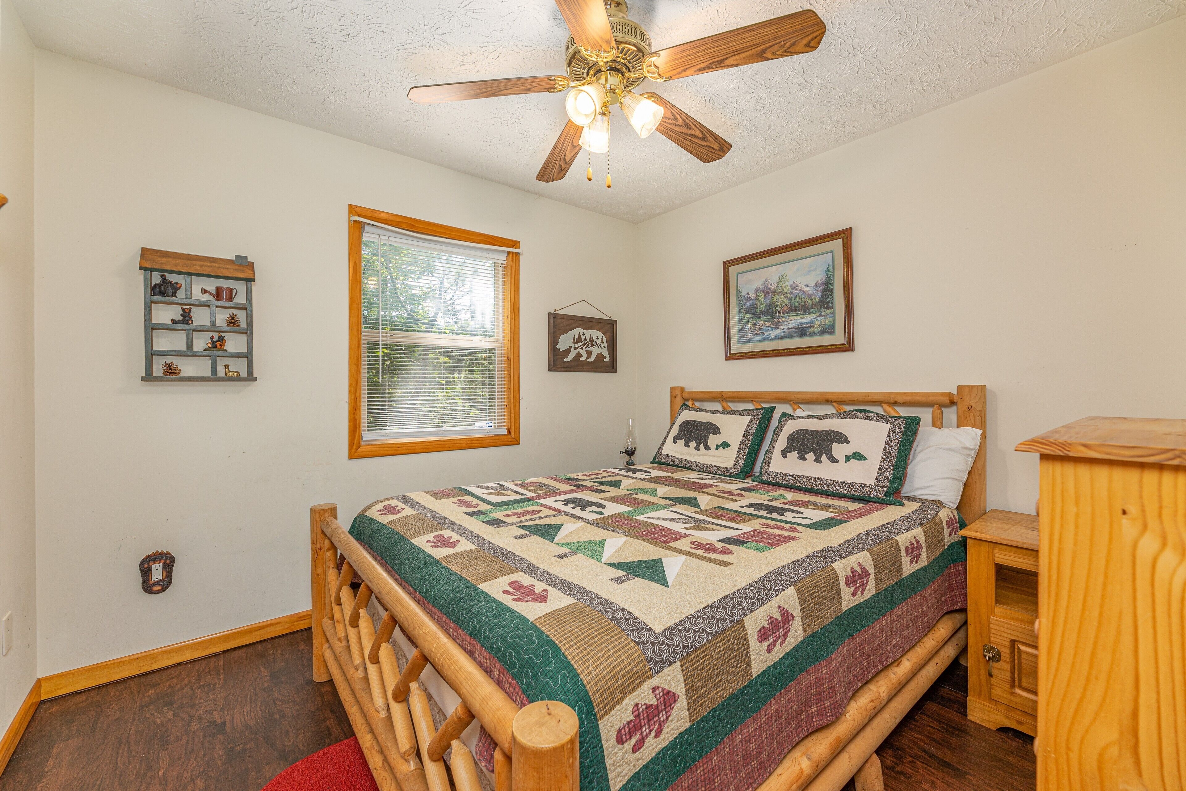 A bedroom with a wooden bed, a ceiling fan, a quilt, a window, and a wall-mounted shelf.