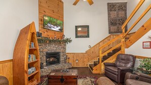 Una sala de estar acogedora con chimenea de piedra, estanterías de madera, un sofá confortable y una escalera.