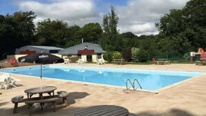 A swimming pool with lounge chairs and a picnic table in the foreground. - Holiday Cabin Sleeps 5 Caernarfon, Snowdonia (Caernarfon)
