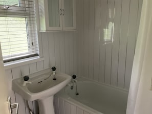 Een badkamer met een witte wastafel, een badkuip en een raam met zonwering.