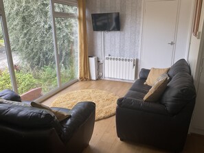 Een woonkamer met een groot raam, een flatscreen televisie, een radiator en een bank.