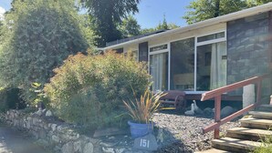 A modern building with a stone wall, a blue planter with a sign '151', and a wooden bench. - Holiday Cabin Sleeps 5 Caernarfon, Snowdonia (Caernarfon)
