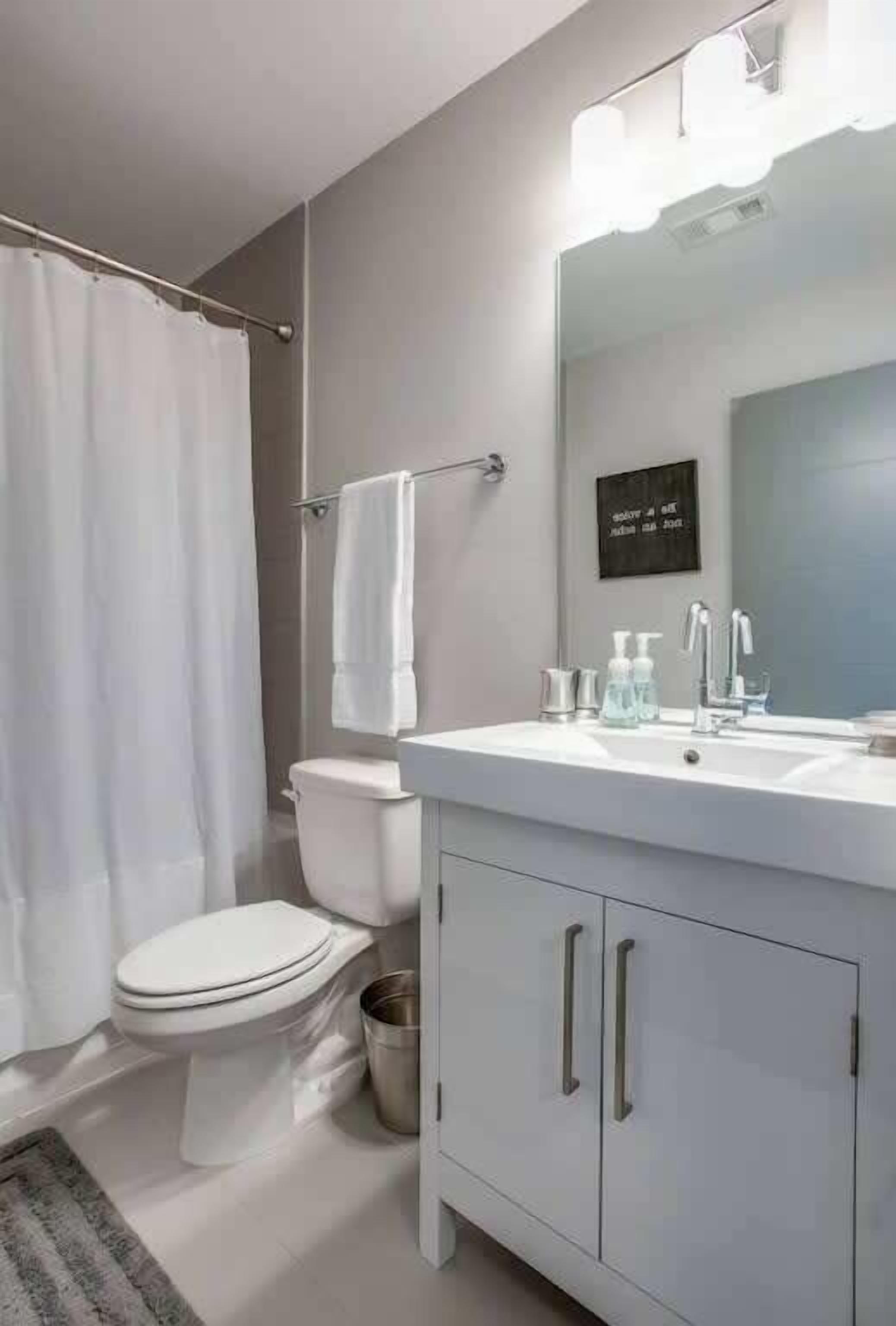 Un baño moderno con lavamanos, espejo y retrete blancos.