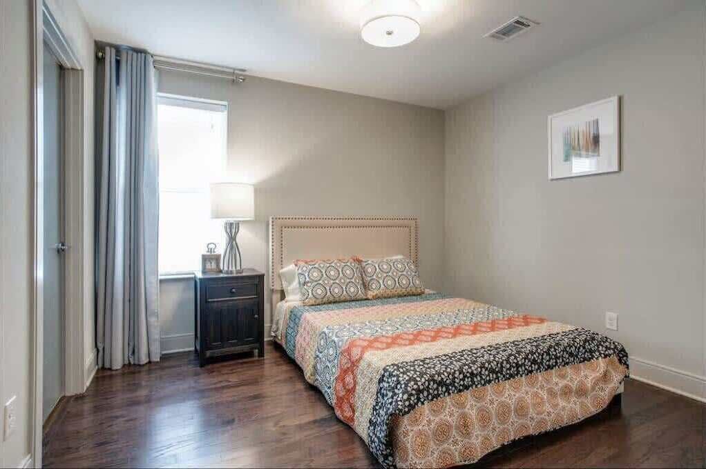 A bedroom with a bed, a nightstand, a lamp, and a window with curtains.