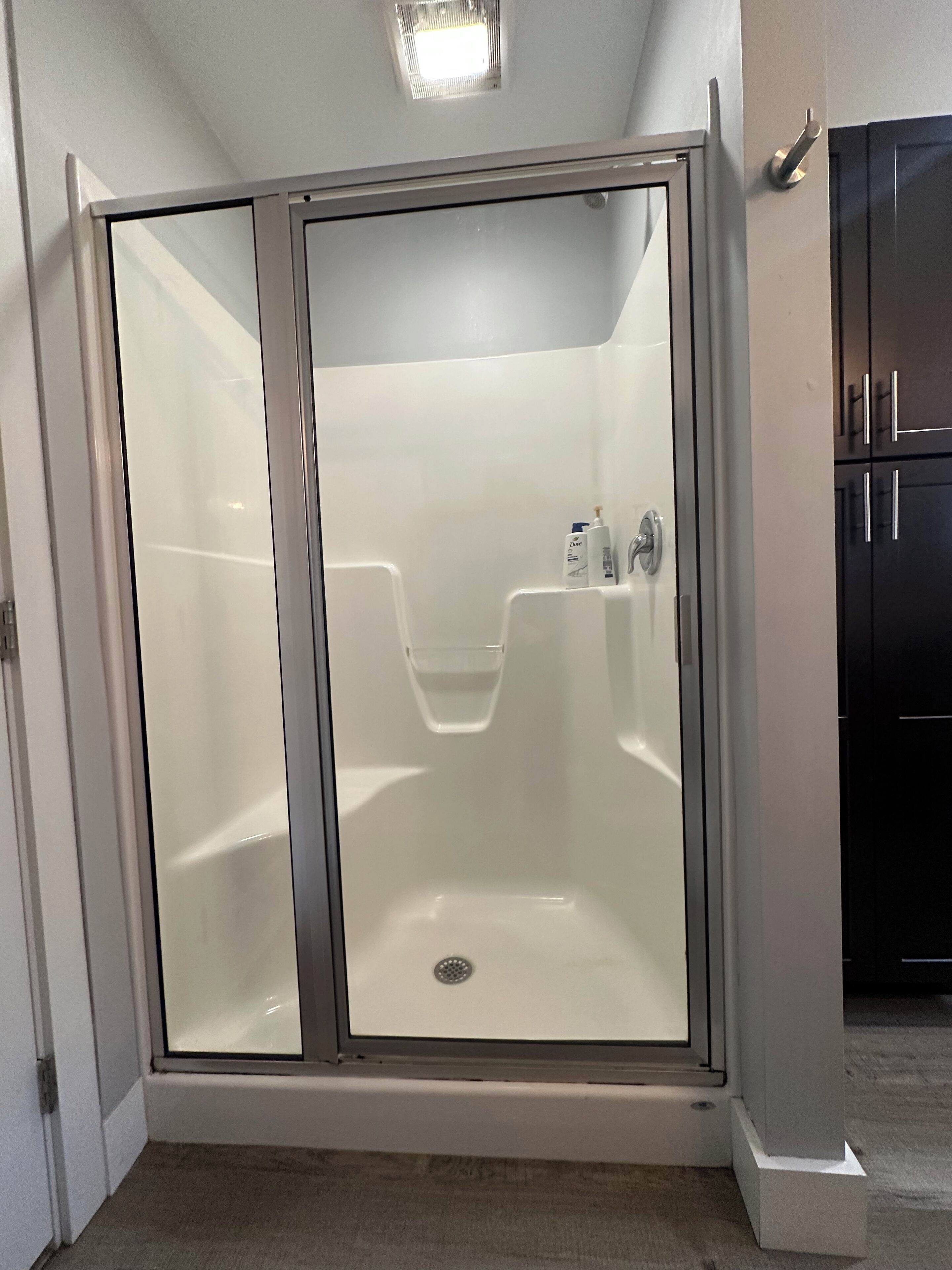 A walk-in shower with a glass door, a showerhead, and a small shelf with toiletries.