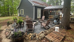 En hytte med en terrasse, Adirondack-stole, grill og en pejsesten.