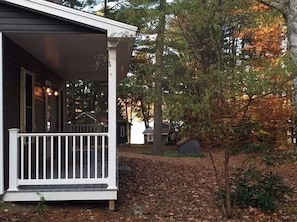 Situated in a secluded natural setting, this single-story home features a charming covered porch with a white railing.