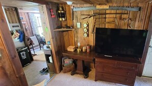 A wooden-paneled room with a large flat-screen TV on a wooden dresser, a shelf with various items, and a door with a white frame.