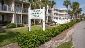 Hotelli nimeltä Grand Caribbean West, jossa on kyltti, useita parvekkeita, palmuja ja päällystetty kävelyreitti.