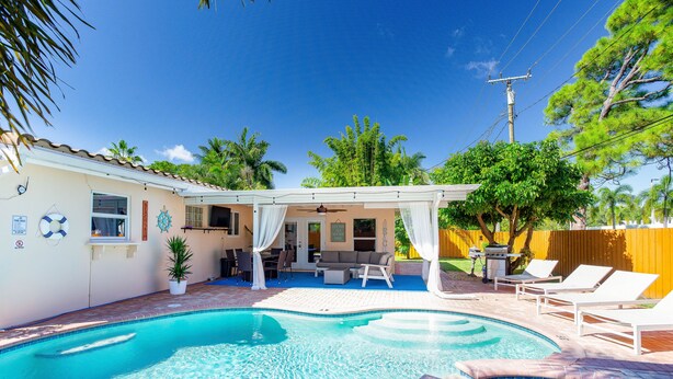 Um quintal com piscina, móveis de pátio e área de estar coberta.