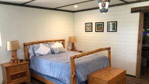 Un lit à baldaquin en bois, accompagné d’une table de chevet et d’une commode assorties, d’une lampe suspendue et de trois tableaux encadrés accrochés au mur.