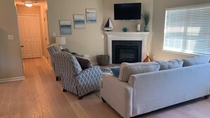 A living room with a fireplace, a television mounted on the wall, and a window with blinds. - Sea You Soon- 1 mile to Camp Lejeune! Monthly rental- fully furnished!  (Hubert)