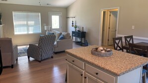 A spacious living room with a large window, a sofa, and a dining area with a table and chairs. - Sea You Soon- 1 mile to Camp Lejeune! Monthly rental- fully furnished!  (Hubert)