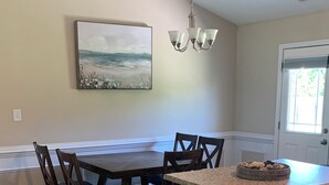 A dining area with a wooden table and chairs, a chandelier, and a painting on the wall. - Sea You Soon- 1 mile to Camp Lejeune! Monthly rental- fully furnished!  (Hubert)