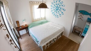 Un dormitorio con cama, suelo de madera, ventana con cortinas, lámpara colgante y decoración en la pared.