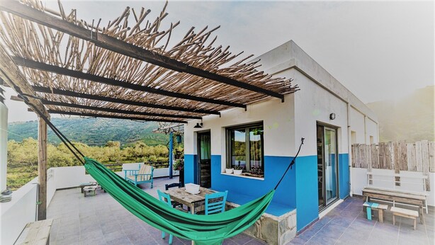 Una casa moderna con fachada azul y blanca, un porche cubierto con una hamaca, una mesa y sillas.