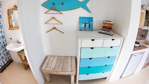 Una habitación con un lavabo blanco, un taburete de madera y un aparador blanco con cajones azules.