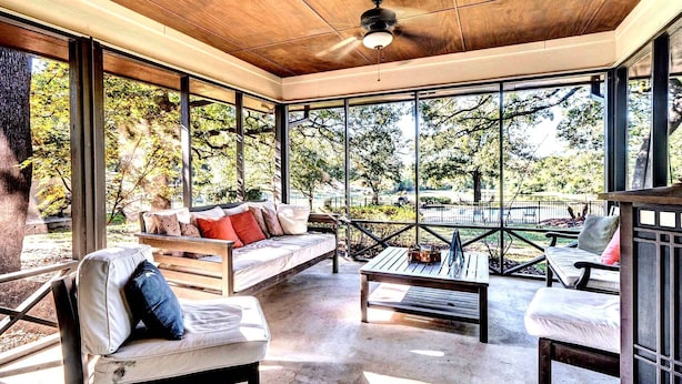 Una habitación iluminada por el sol, con techo de madera, ventanas amplias y una zona de estar con sofá y sillones.