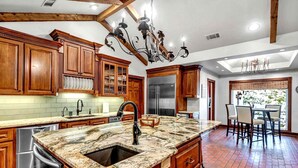 Una cocina con armarios de madera, encimera de granito, electrodomésticos de acero inoxidable y una araña.