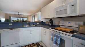 Een moderne keuken met witte kastjes, een magnetron, een fornuis en een koffiezetapparaat.