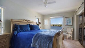 Een slaapkamer met een groot bed, een stoel, een plafondventilator en uitzicht op zee.