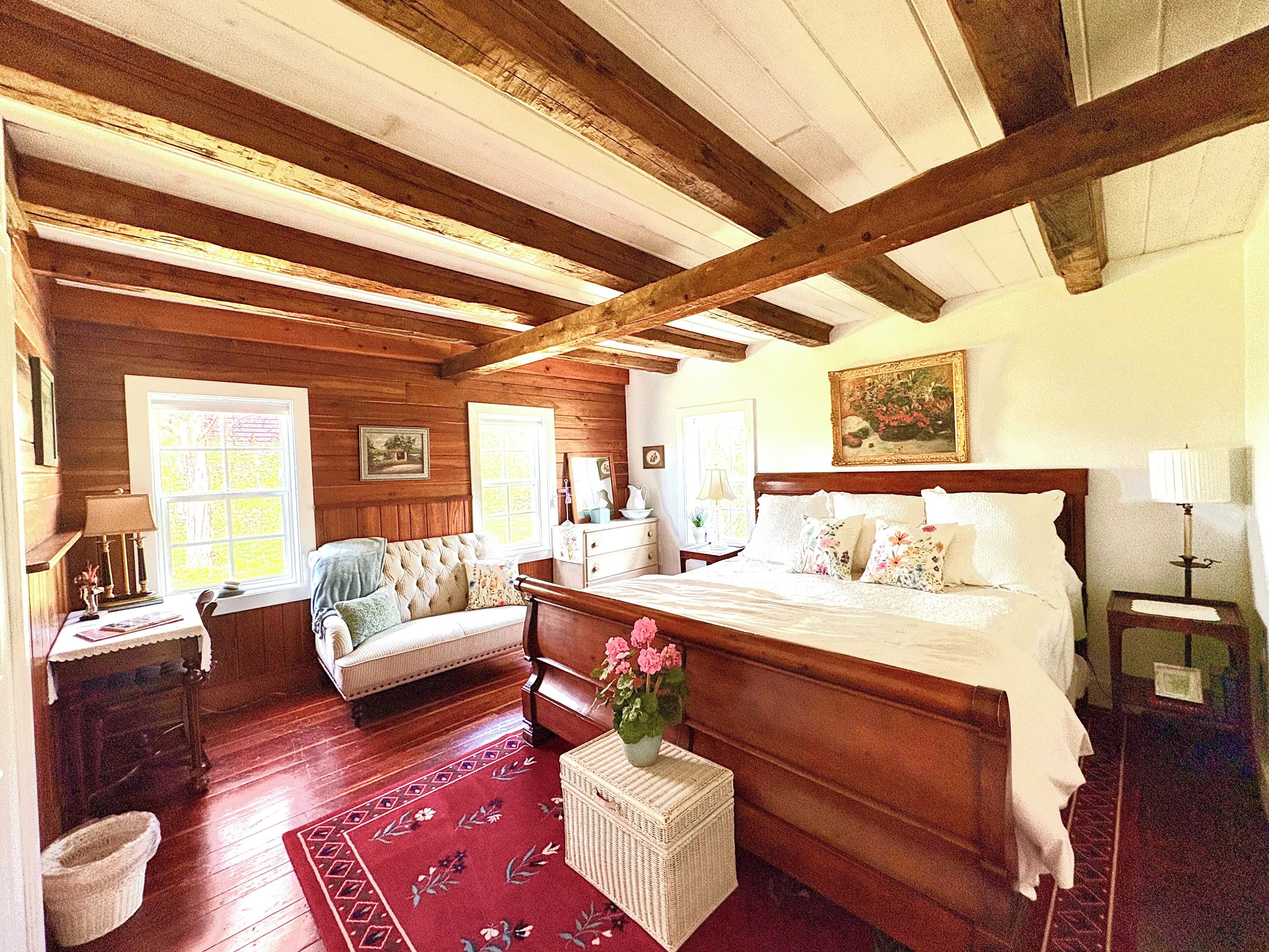 Un dormitorio con techo de madera, una cama grande, un aparador, una silla y una ventana.