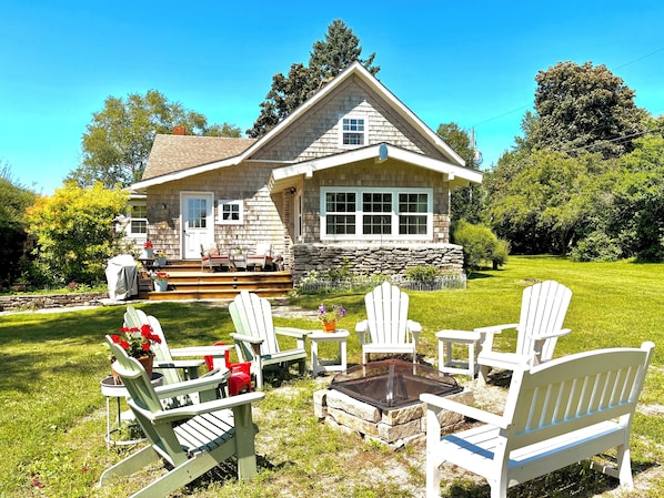 A house with a stone foundation, a porch with outdoor seating, and a fire pit in the yard. - Located in Ephraim, in the heart of Door County (Sister Bay)