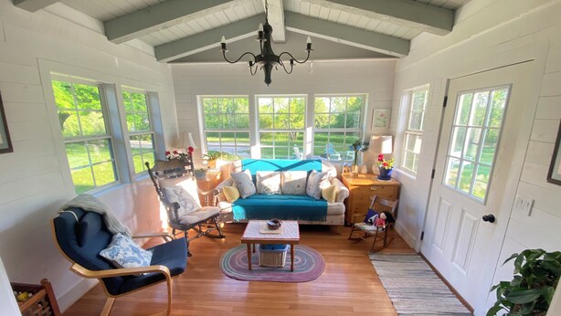 A spacious living room with a high ceiling, wooden flooring, and large windows offering a view of the outdoors. - Located in Ephraim, in the heart of Door County (Sister Bay)