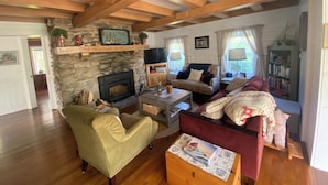 A cozy living room with a stone fireplace, wooden beams, a sofa, a chair, and a bookshelf. - Located in Ephraim, in the heart of Door County (Sister Bay)