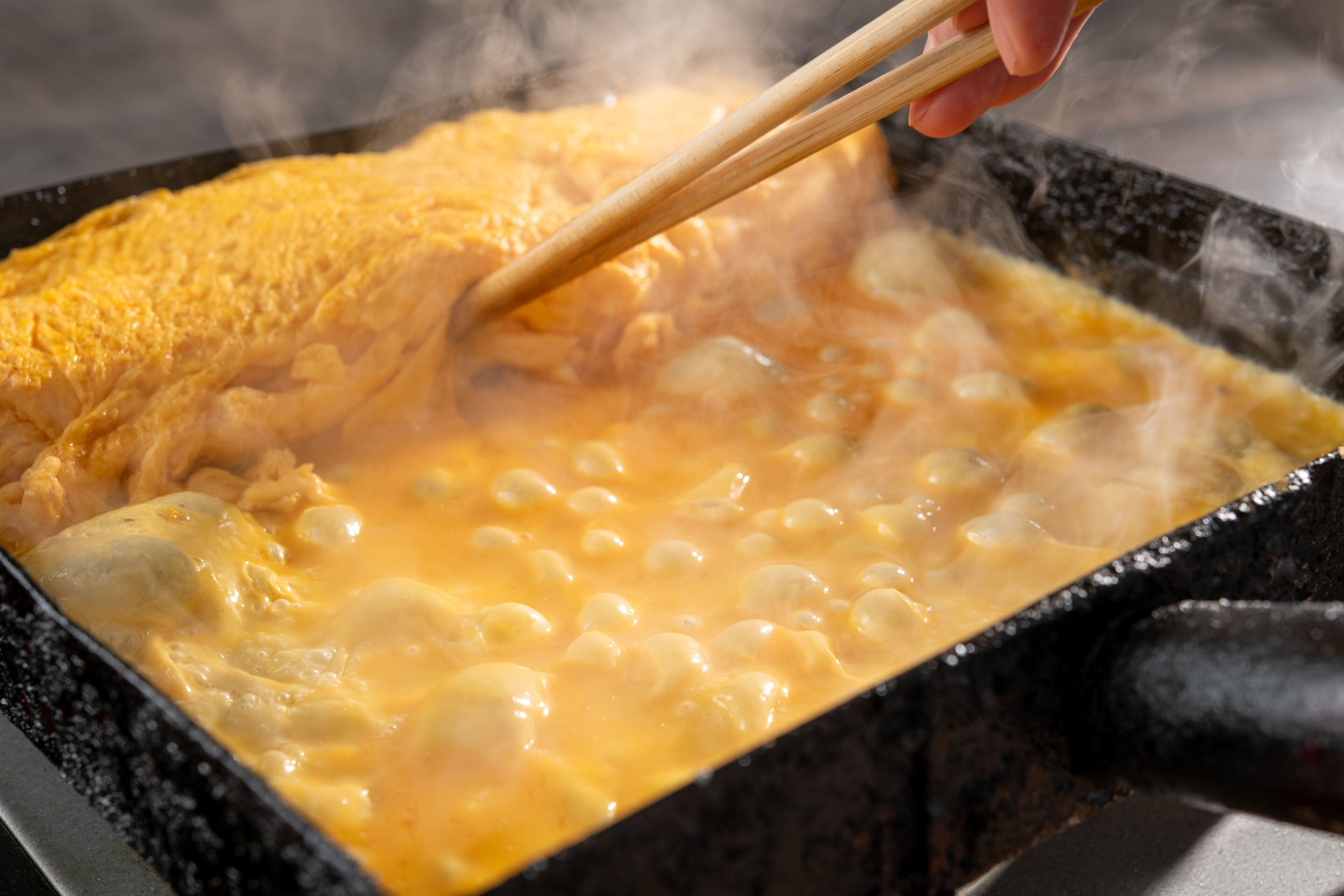 A close-up of a hot pot with a hand using chopsticks to stir the contents.