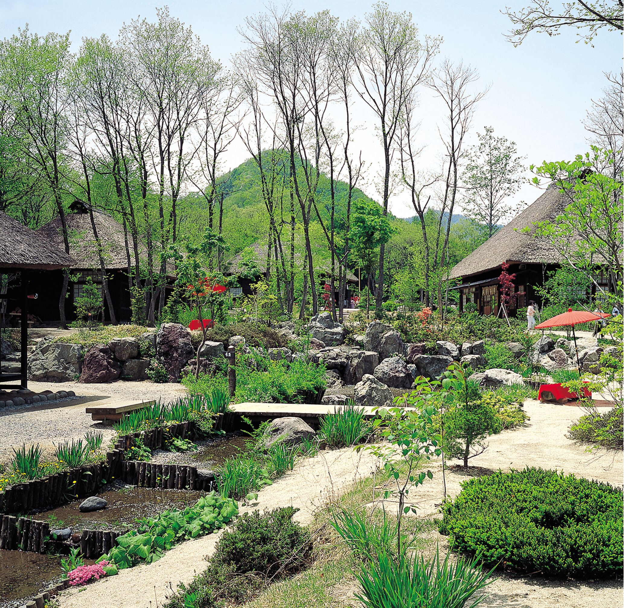 A garden with rock formations, a pond, and traditional wooden structures.