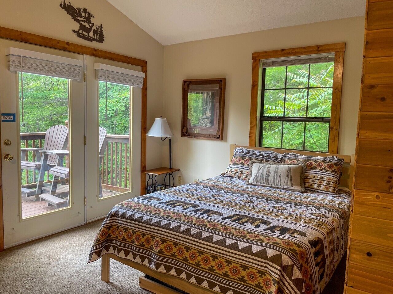 A bedroom with a large bed, a nightstand, a lamp, and a window with a view of greenery.