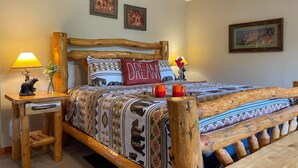 A bedroom with a wooden bed frame, a nightstand with a lamp, and two wall-mounted pictures. - Romantic Private Cabin | Hot Tub | Mtn Views, Pets (Sevierville)