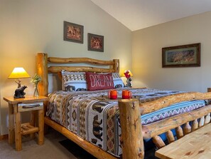 A bedroom with a wooden bed frame, a nightstand with a lamp, and two wall-mounted pictures. - Romantic Private Cabin | Hot Tub | Mtn Views, Pets (Sevierville)