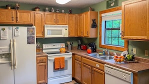 A kitchen with wooden cabinets, a white refrigerator, a stove, a sink, and a window. - Romantic Private Cabin | Hot Tub | Mtn Views, Pets (Sevierville)
