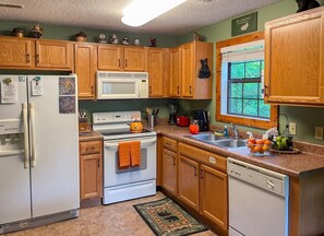 A kitchen with wooden cabinets, a white refrigerator, a stove, a sink, and a window. - Romantic Private Cabin | Hot Tub | Mtn Views, Pets (Sevierville)
