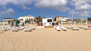 A beach with rows of sun loungers and a few buildings in the background.