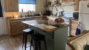 Eine Küche mit Holzausstattung, einer Kochinsel mit Barhocker, einer Mikrowelle, einem Kühlschrank und diversen Küchengeräten.