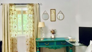 Ein Schlafzimmer mit einem Bett, einem Schreibtisch mit Lampe, einer Vase mit Blumen und einem Fernseher.