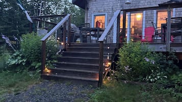 Een houten huis met veranda en buiten zitplaatsen, omgeven door groen.